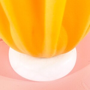 May include: A bright yellow ceramic pumpkin with a white base. The pumpkin has a smooth, rounded shape and a slightly textured surface.