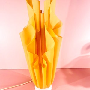 May include: A yellow table lamp with a unique, pleated, folded fabric shade. The lamp has a white base.