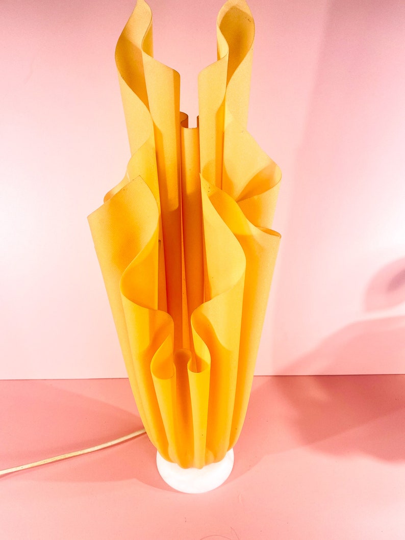 May include: A yellow table lamp with a unique, pleated, folded fabric shade. The lamp has a white base.