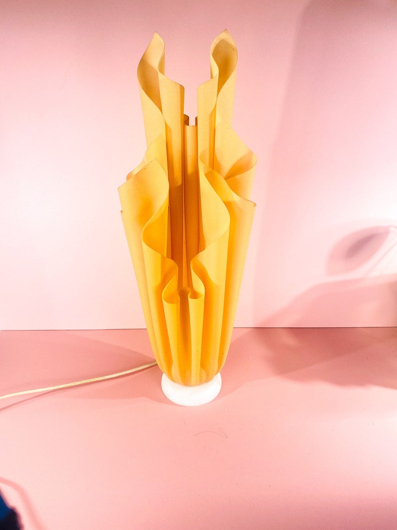 May include: A yellow, pleated lamp with a white base. The lamp is shaped like a flower and has a modern design.