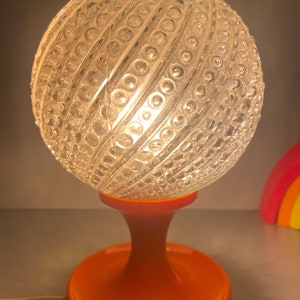 May include: A vintage orange table lamp with a clear glass globe shade. The globe has a textured pattern of small circles.