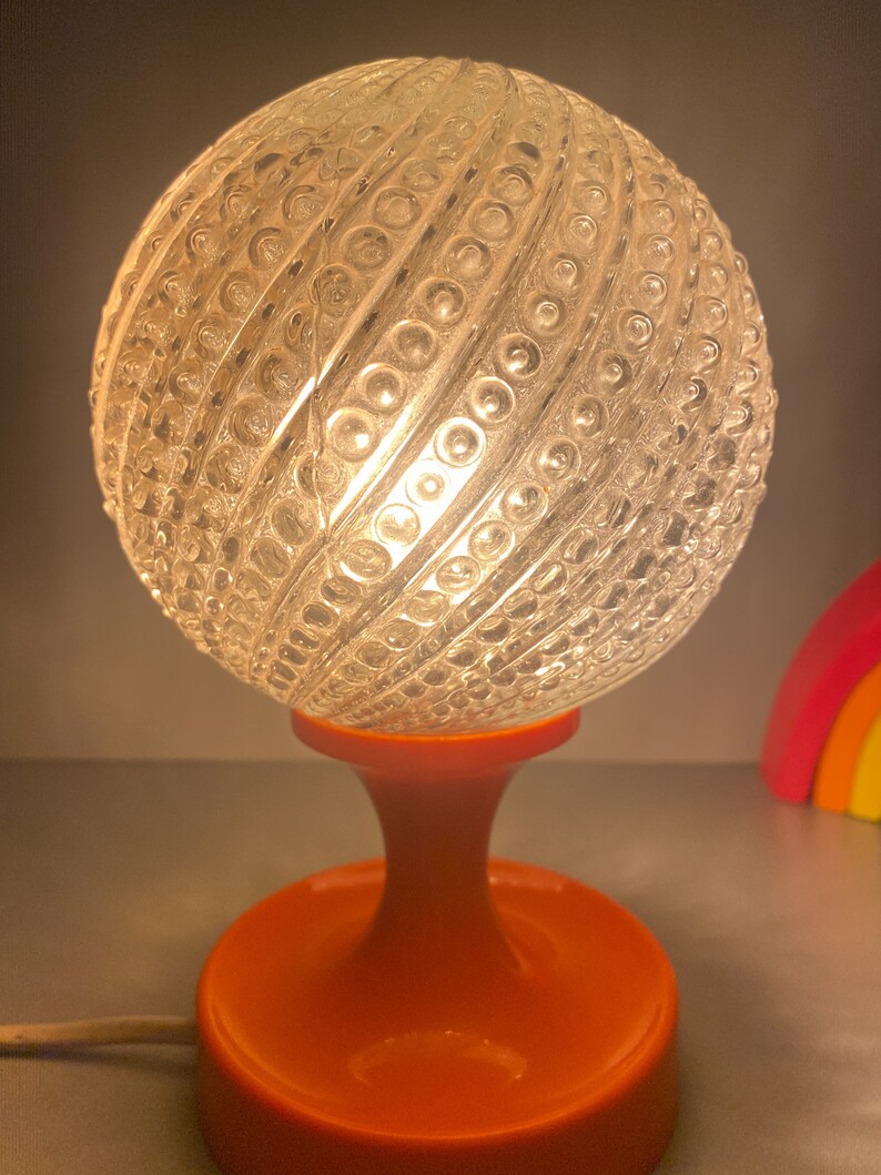May include: A vintage orange table lamp with a clear glass globe shade. The globe has a textured pattern of small circles.