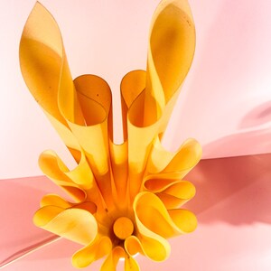 May include: A yellow, folded paper lampshade with a unique, organic design. The lampshade is made of multiple layers of paper that are folded and curved to create a flowing, wave-like effect.