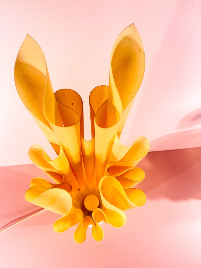 May include: A yellow, folded paper lampshade with a unique, organic design. The lampshade is made of multiple layers of paper that are folded and curved to create a flowing, wave-like effect.