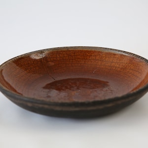 May include: A brown ceramic bowl with a dark brown rim. The bowl has a crack in the glaze.