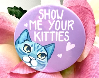 Könnte beinhalten: Lilafarbener Knopf mit dem Text "Show me your kitties" in Weiß. Eine blaue getigerte Katze aus einem Cartoon mit gelben Augen schaut von der linken Seite des Knopfes heraus. Auf dem Knopf befinden sich drei rosa Herzen.