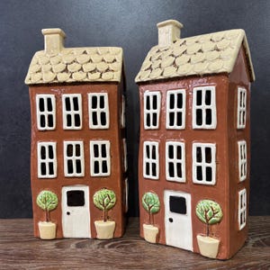May include: Two ceramic houses with white trim and windows, brown brick walls, and green trees. The houses have white doors and a cream-coloured roof.