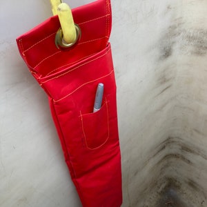 May include: A red canvas tool bag with a yellow strap and a small pocket. A pen is in the pocket.