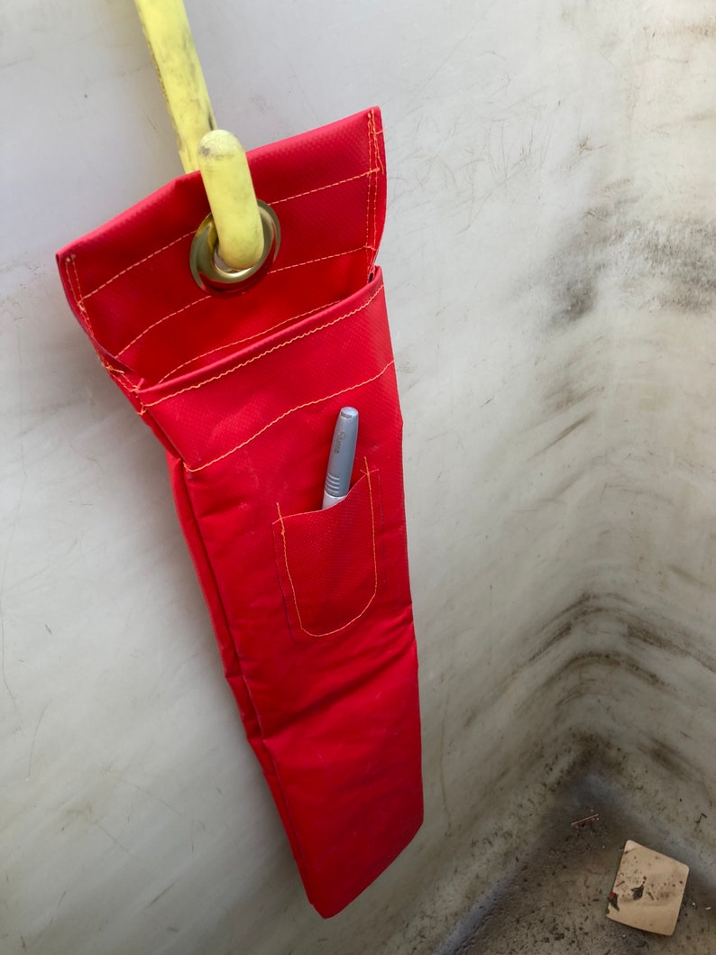 May include: A red canvas tool bag with a yellow strap and a small pocket. A pen is in the pocket.