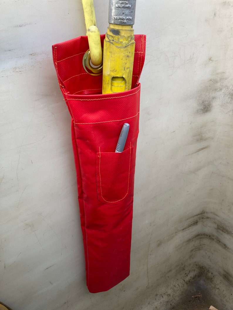 May include: A red canvas tool bag with a yellow and silver tool inside. The bag has a small pocket on the front with a pen inside.