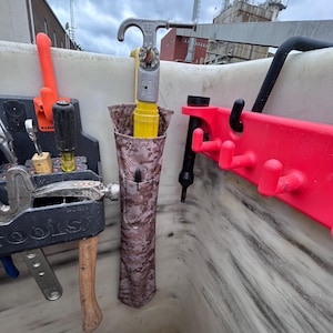 Pu&ograve; includere: Una collezione di strumenti e attrezzature, tra cui un martello, chiavi inglesi e uno strumento giallo e argento, sono conservati in un contenitore bianco. &Egrave; visibile anche un rack rosso con ganci. Gli strumenti sono organizzati per un facile accesso.