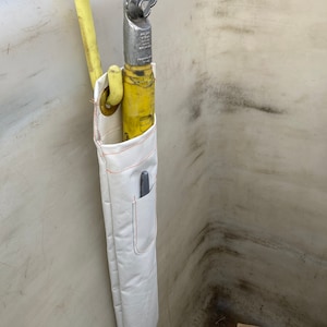 K&ouml;nnte beinhalten: Ein gelbes und silbernes Feuerwehrwerkzeug mit einer wei&szlig;en Segeltuchscheide. Das Werkzeug hat einen Haken und ein spitzes Ende. Die Scheide hat eine Tasche mit einem Stift darin. Das Werkzeug h&auml;ngt an einer wei&szlig;en Oberfl&auml;che.