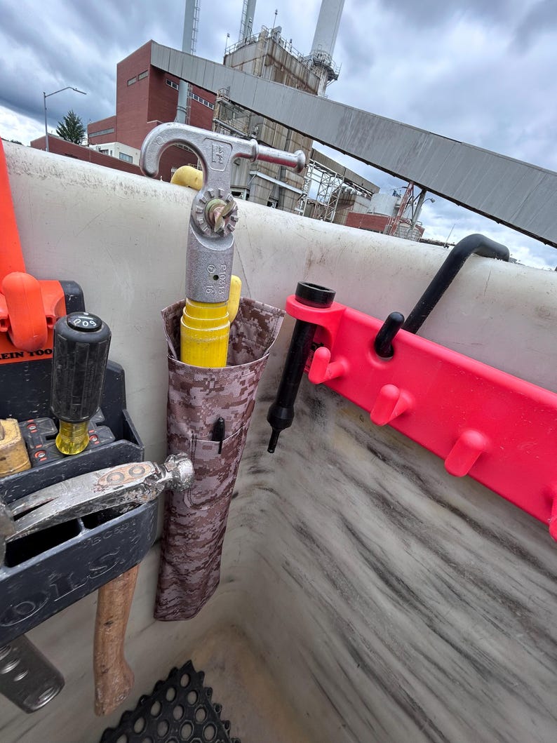 Pu&ograve; includere: Una collezione di strumenti, tra cui un martello, un cacciavite e una chiave inglese, &egrave; visibile in un'area di lavoro. Un porta attrezzi mimetico contiene un tubo giallo e una penna. &Egrave; presente anche un supporto in plastica rossa con ganci.