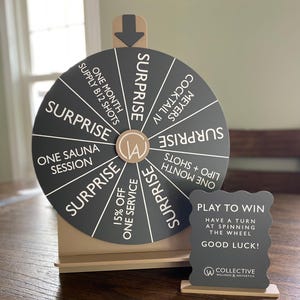 Peut inclure: Une roue de loterie noire et blanche avec diverses options de services de bien-être. La roue comprend du texte tel que "Surprise", "Une séance de sauna" et "Cocktail IV Meyers". Un petit panneau indique "Jouez pour gagner" et "Bonne chance!"