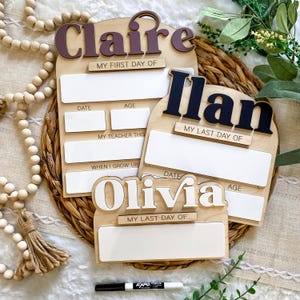 May include: Wooden school boards with names Claire, Ilan, and Olivia in various colors. Each board has space for date, age, and teacher information. The boards are on a woven mat with a black marker.