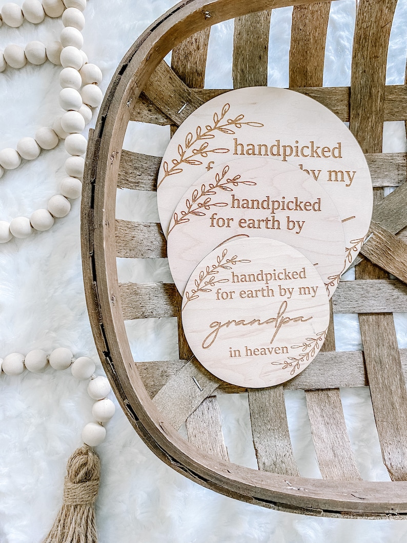 Peut inclure: Trois cercles en bois avec le texte "handpicked for earth by" sur le cercle du haut, "handpicked for earth by my grandpa" sur le cercle du bas et "handpicked by my" sur le cercle du milieu. Les cercles sont dans un panier en bois.