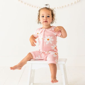 May include: A pink baby onesie with a white daisy print. The onesie has a zipper closure and short sleeves.