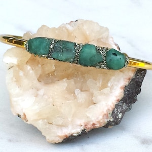 May include: Gold bangle bracelet with a row of green emerald stones set in gold.