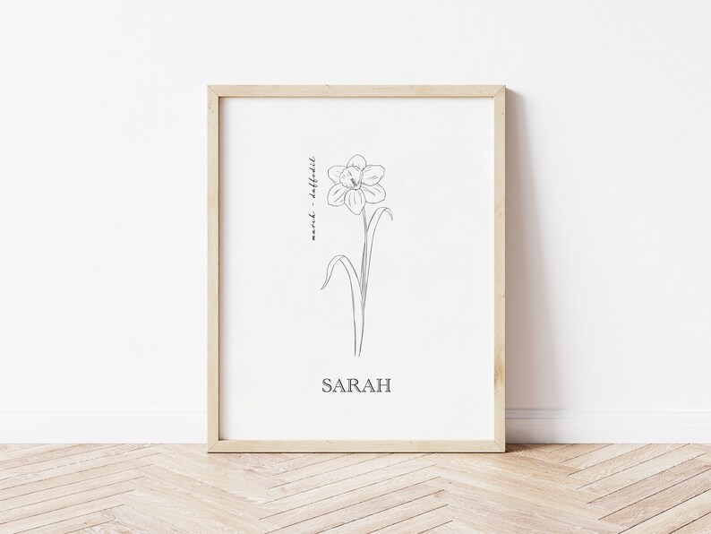 May include: A framed print with a black and white line drawing of a daffodil flower. The text "Daffodil -  and" is written vertically along the stem of the flower. The name "SARAH" is written below the flower.