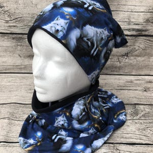 Könnte beinhalten: Ein blaues und weißes Wintermützen- und Halssocken-Set mit einem weißen Wolf-Druck. Die Mütze ist ein Beanie-Stil mit einem umgeschlagenen Bündchen. Der Halssocken ist ein Cowl-Stil.