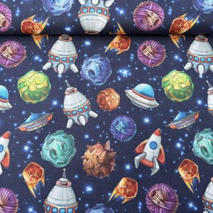 Könnte beinhalten: Ein marineblauer Stoff mit einem sich wiederholenden Muster aus bunten Planeten, Sternen und Raumschiffen. Die Planeten sind in verschiedenen Formen und Größen, und die Raumschiffe sind in verschiedenen Stilen.