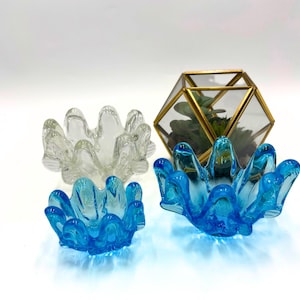 May include: Three glass bowls, two are blue and one is clear. The blue bowls have a wavy, organic shape. The clear bowl has a similar shape but is more rounded. The bowls are arranged on a white surface.