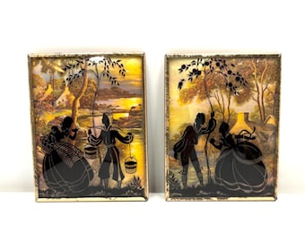 May include: Two framed vintage silhouette art pieces. Each features a black silhouette of figures in a pastoral scene, set against a colorful landscape with a house and trees. The frames have a gold-colored trim.