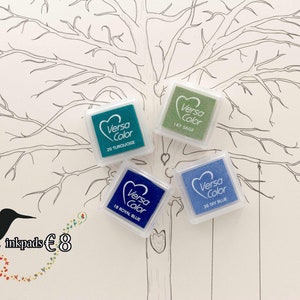 Könnte beinhalten: Vier Stempelkissen in einem Set, mit dem Markennamen "Versa Color" und den Farbnamen "Türkis", "Königsblau", "Salbei" und "Himmelblau". Die Stempelkissen sind auf einer weißen Oberfläche mit einer Baumzeichnung im Hintergrund angeordnet. Der Text "4 inkpads €8" ist in der linken unteren Ecke des Bildes sichtbar.