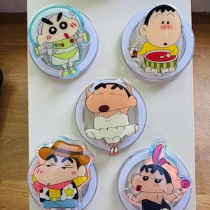 May include: A collection of five cartoon character-themed acrylic magnets. Each magnet features a different character in various costumes, including a cowboy, a ballerina, and a space suit. The magnets are set against a white background.