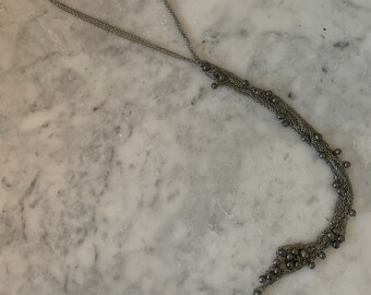 Könnte beinhalten: Eine silberfarbene Halskette mit mehreren Strängen und kleinen, dunkelgrauen Perlen. Die Halskette hat ein langes, kaskadierendes Design mit einer Ansammlung von Perlen am unteren Ende. Die Kette ist filigran und scheint aus Metall zu sein.