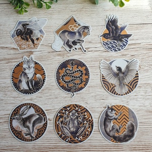 May include: Set of ten illustrated stickers featuring various animals and nature scenes. The stickers are round and feature a white background with gold accents. The animals include a fox, a snake, a frog, a bird, a rabbit, a horse, a bee, and a crow.