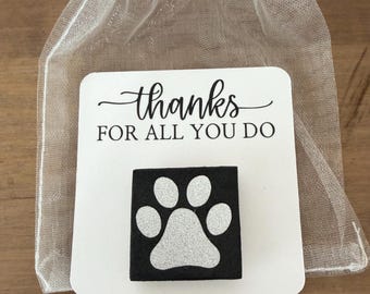 May include: A square black pin featuring a silver glitter paw print design, attached to a white card with the text "thanks FOR ALL YOU DO" in black, all contained within a sheer white organza drawstring gift bag.