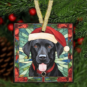 May include: Square Christmas ornament featuring a black Labrador Retriever wearing a Santa hat and red collar. The dog's portrait is set against a stained-glass style background with red and green accents. A gold ribbon is attached for hanging.