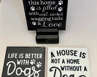 May include: A black and white dog-themed decor set. Includes a black holder with the text "this home is filled with wet noses wagging tails & Love". Also includes two square tiles with dog-related quotes and paw prints.