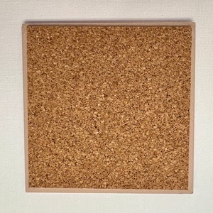 May include: Square cork coaster with a light brown border. The coaster's surface is a textured, light brown cork material. The coaster is set against a white background.
