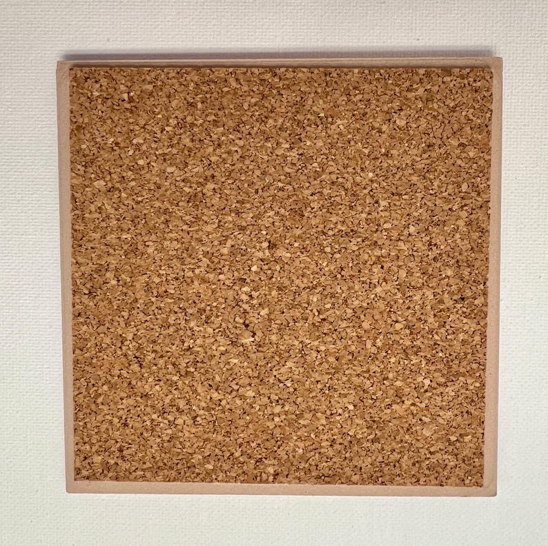May include: Square cork coaster with a light brown border. The coaster's surface is a textured, light brown cork material. The coaster is set against a white background.