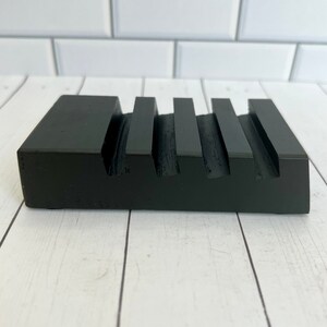 May include: A black wooden soap dish with a rectangular shape and four parallel grooves. The dish is made of solid wood and has a matte finish. The design is simple and modern, suitable for a bathroom or kitchen.
