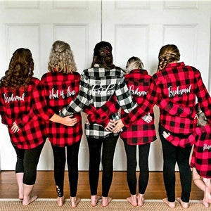 May include: Six people wearing red and black plaid shirts with white text on the back. The text reads "Bride", "Maid of Honor", "Bridesmaid", and "Bridesmaid".