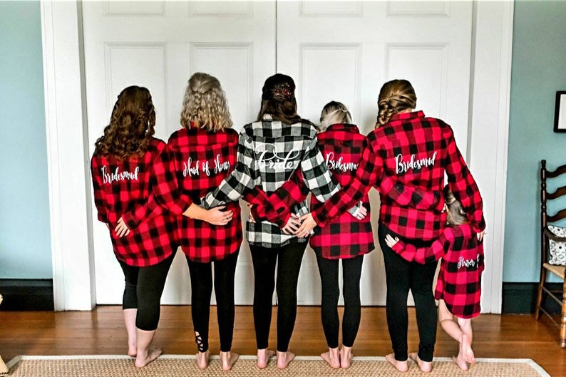 May include: Six people wearing red and black plaid shirts with white text on the back. The text reads "Bride", "Maid of Honor", "Bridesmaid", and "Bridesmaid".