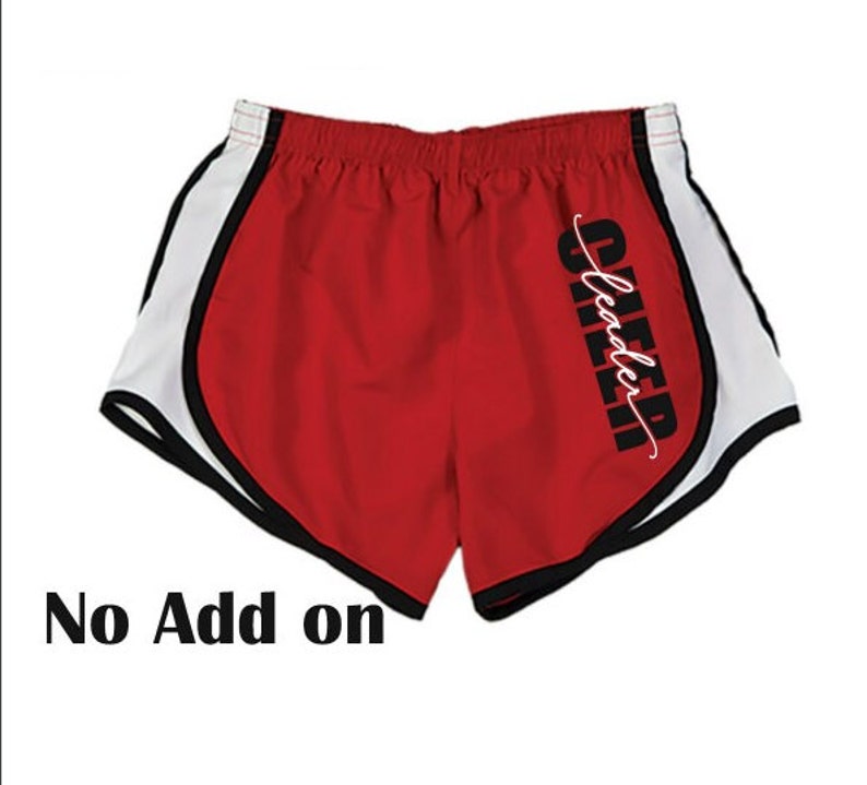 Op de afbeelding: Rode hardloopshorts met witte en zwarte bies. De shorts hebben het woord "CHEER" verticaal op het rechterbeen geschreven met het woord "leader" eronder in cursief.