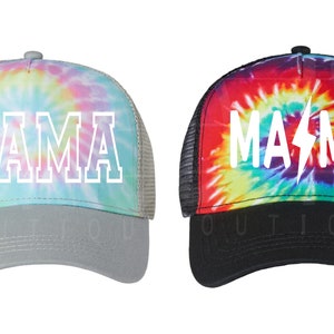 May include: Two tie-dye trucker hats with the word "MAMA" written in white on the front. The hat on the left has a pastel tie-dye pattern and a gray mesh back. The hat on the right has a red, orange, yellow, green, blue, and purple tie-dye pattern and a black mesh back. The hat on the right also has a lightning bolt in the word "MAMA".