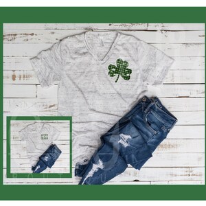 May include: A white t-shirt with a green shamrock design and the text "Lucky Charm" on a white t-shirt. The t-shirt is paired with blue jeans.