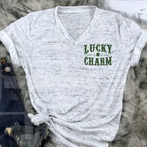 May include: White t-shirt with a green shamrock and the text "LUCKY CHARM" printed on the front.