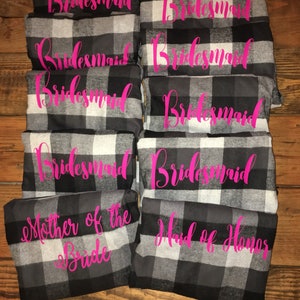 May include: A set of eight black and white plaid robes with pink text. The robes say "bridesmaid", "mother of the bride", and "maid of honor".