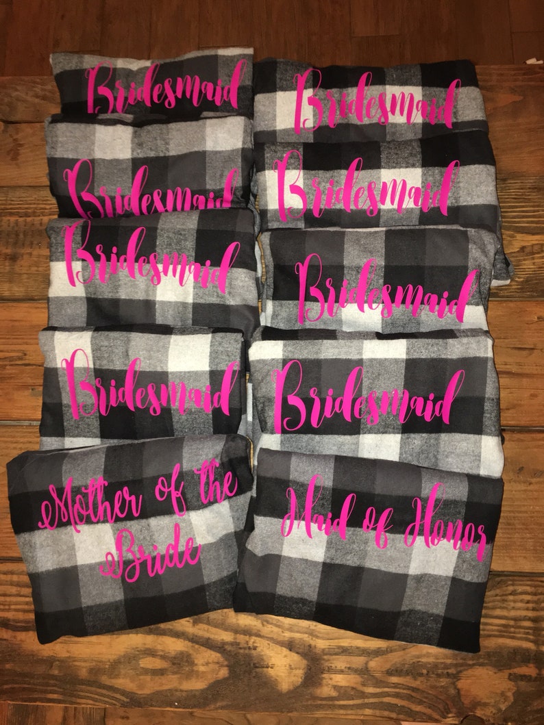 May include: A set of eight black and white plaid robes with pink text. The robes say "bridesmaid", "mother of the bride", and "maid of honor".