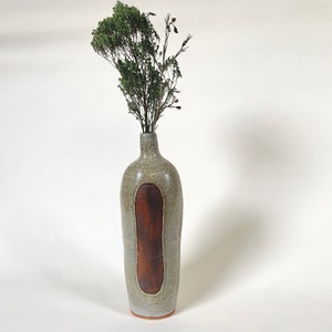 May include: A gray ceramic vase with a brown stripe down the center, holding a bouquet of dried green foliage.