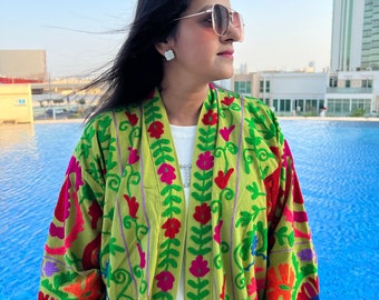 May include: A green embroidered kimono with colorful floral patterns. The kimono has a long sleeve and a V-neckline. The fabric is lightweight and flowy.