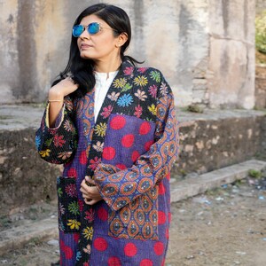 May include: A patchwork kimono-style jacket in a variety of patterns and colors. The jacket features a purple base with large red polka dots, floral and paisley patterns, and black pockets. The sleeves and collar have contrasting designs.