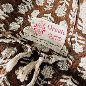 Puede incluir: Una tela marr&oacute;n con un patr&oacute;n floral blanco y una etiqueta blanca que dice "Ornate Handmade with Love www.OrnateHandicrafts.com Made in India"
