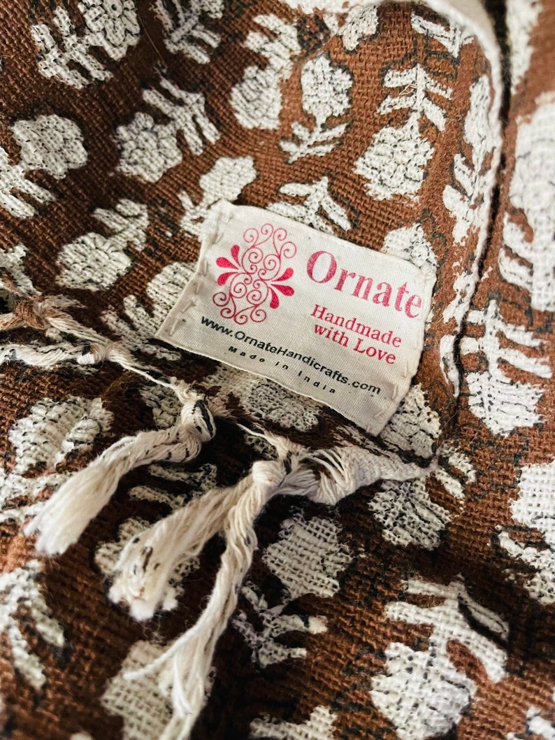 Puede incluir: Una tela marr&oacute;n con un patr&oacute;n floral blanco y una etiqueta blanca que dice "Ornate Handmade with Love www.OrnateHandicrafts.com Made in India"